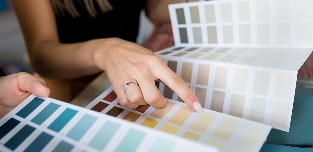 Close-up of hands selecting neutral paint colors from a swatch book &mdash; perfect for staging homes and enhancing curb appeal in real estate listings.
