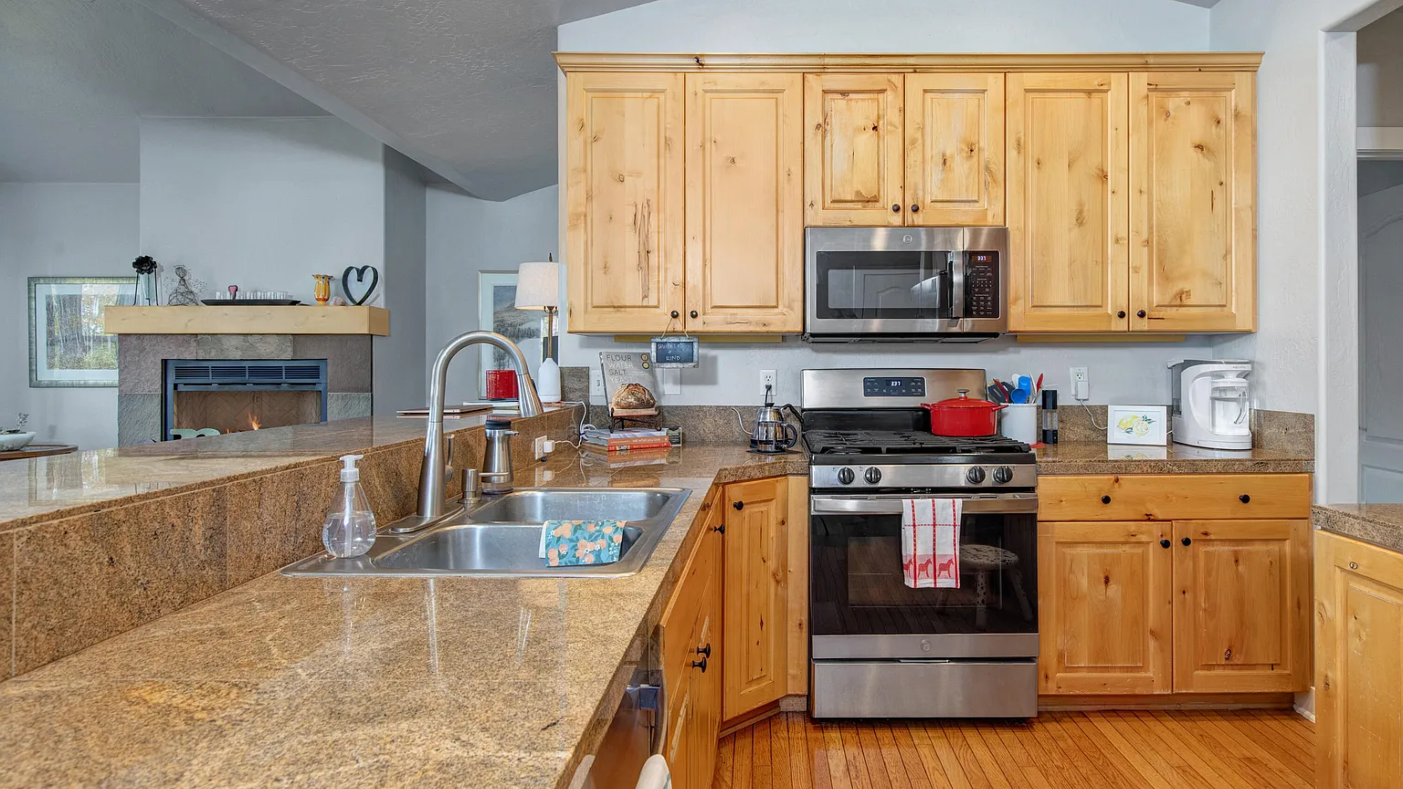 Modern kitchen at 5135 Cove Canyon Dr Park City condo for sale featuring granite countertops, stainless steel appliances, and natural wood cabinetry with open sightlines to the living room fireplace.