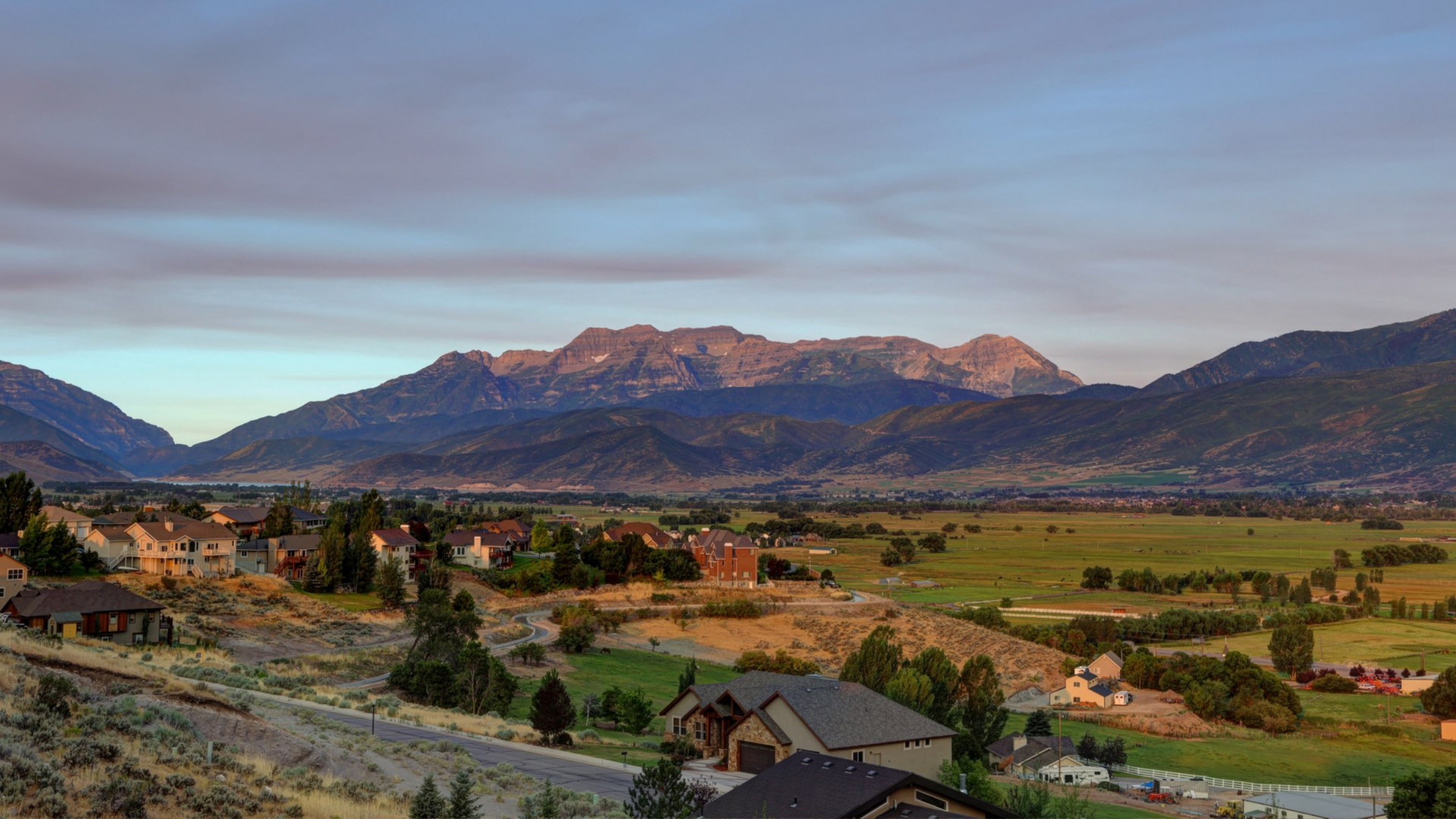 Scenic view of Heber Valley real estate with modern homes, open green spaces, and the Wasatch Mountains in the background, highlighting the area's lifestyle and growth.