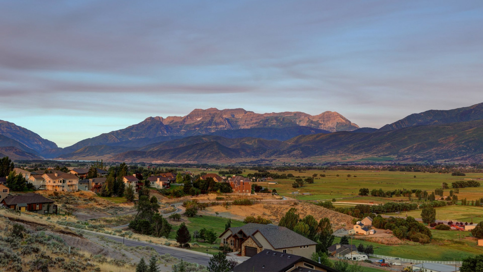Scenic view of Heber Valley real estate with modern homes, open green spaces, and the Wasatch Mountains in the background, highlighting the area's lifestyle and growth.