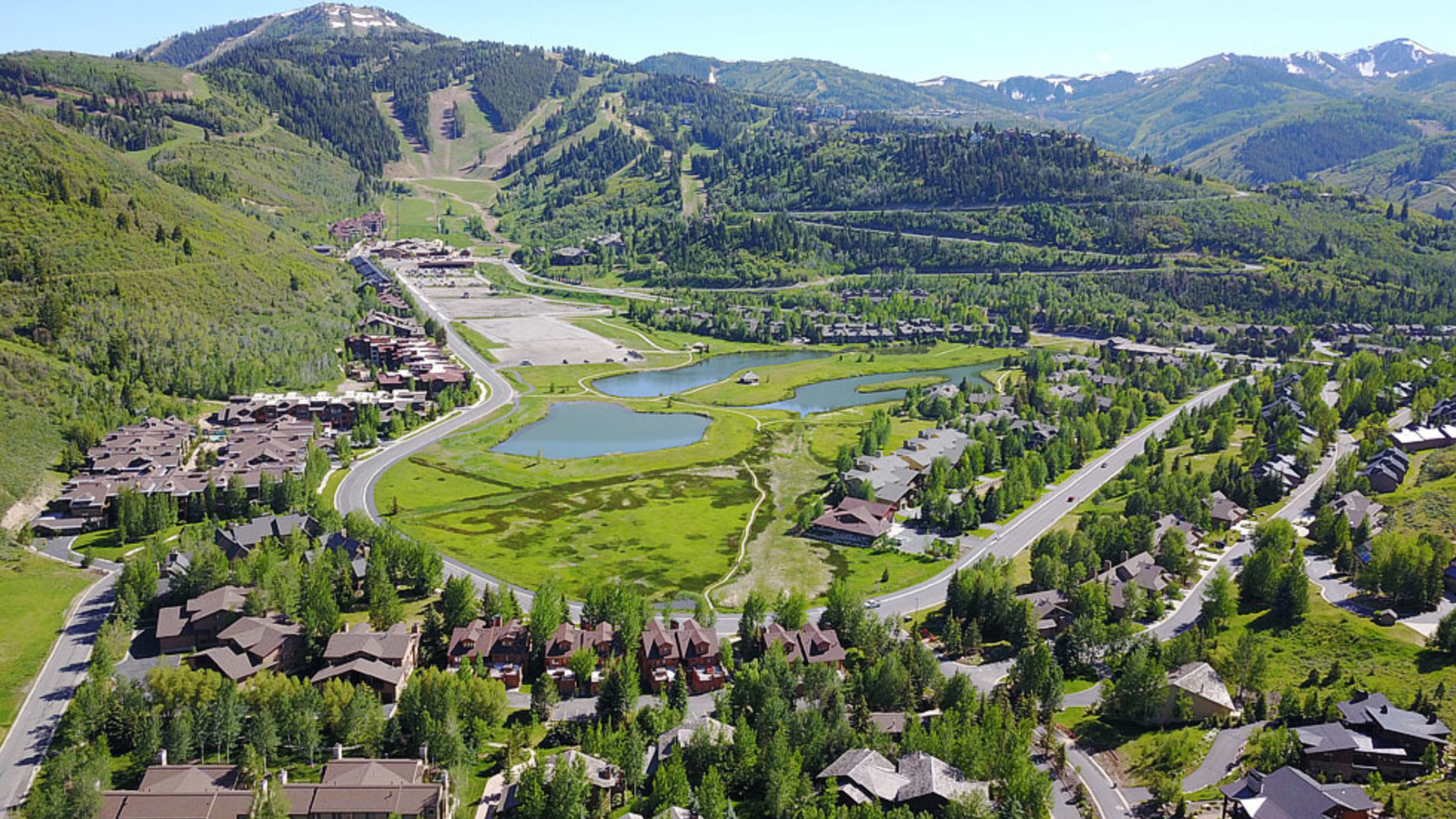 Aerial view of Lower Deer Valley Resort area showcasing luxury homes, scenic ponds, and ski slopes surrounded by lush green mountains in Park City, Utah.