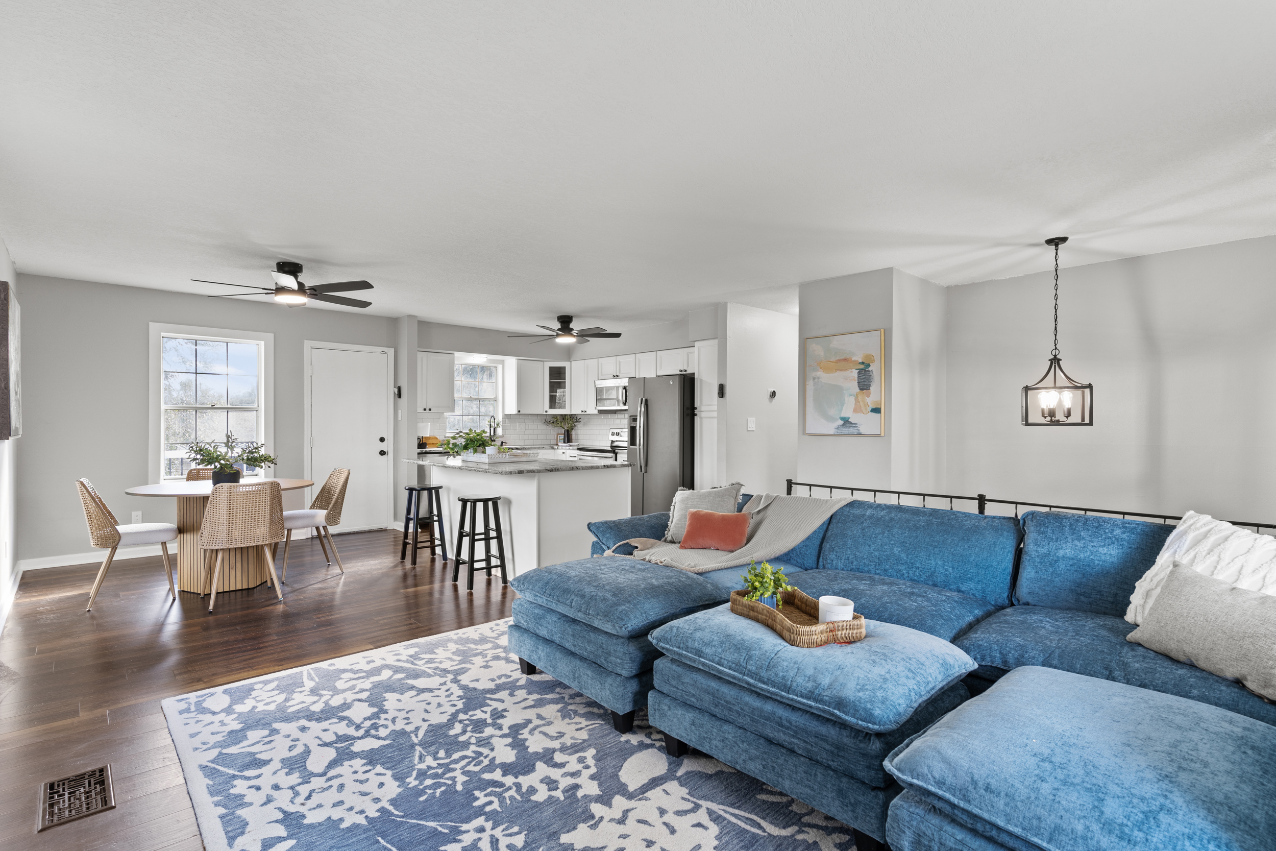 Open-plan living room with a blue sectional, patterned rug, dining area, and white kitchen.